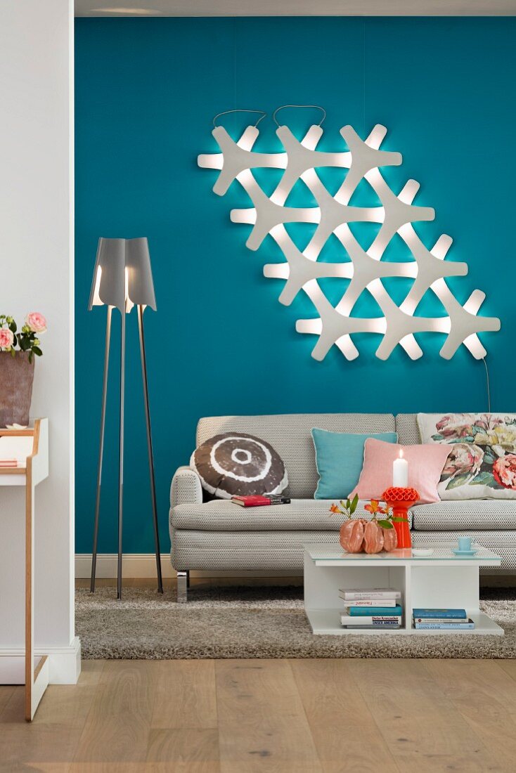 Wohnbereich mit Sofa, Stehlampe & moderner Wandleuchte vor blauer Wand