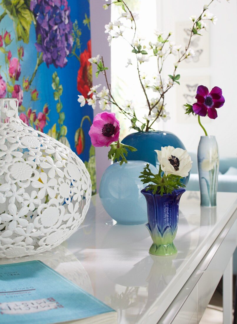 Anemonen und Blütenzweig in Vasen vor einem Dekopaneel mit floralem Design
