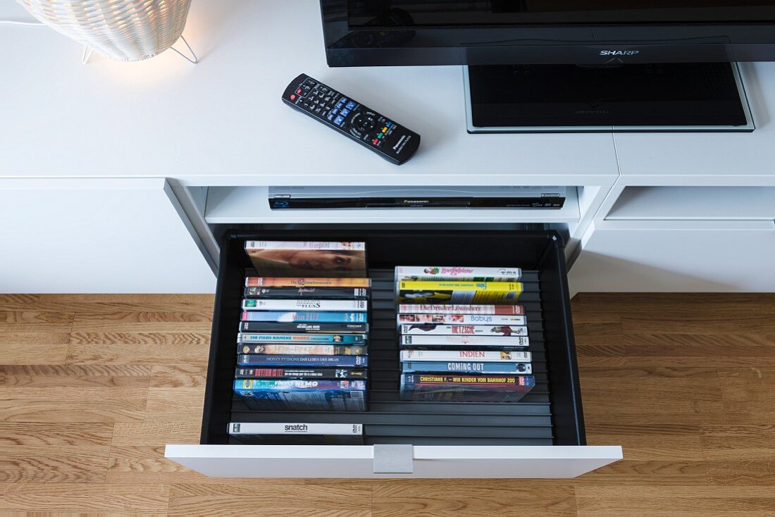 Ausgezogene DVD-Schublade in einem Medienschrank und Flatscreen mit Fernbedienung