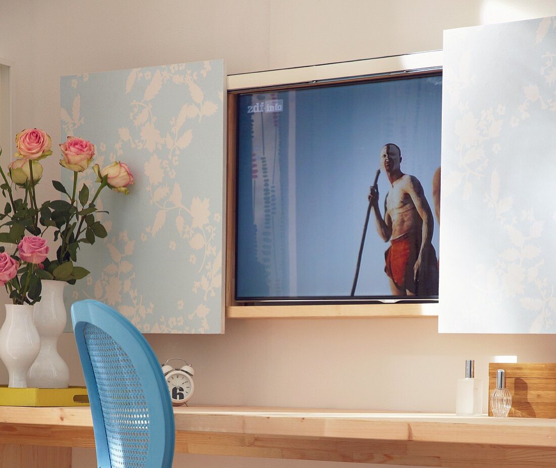 Fernseher hintre tapezierten Schiebetüren, davor Konsolentisch mit Rosenstrauss