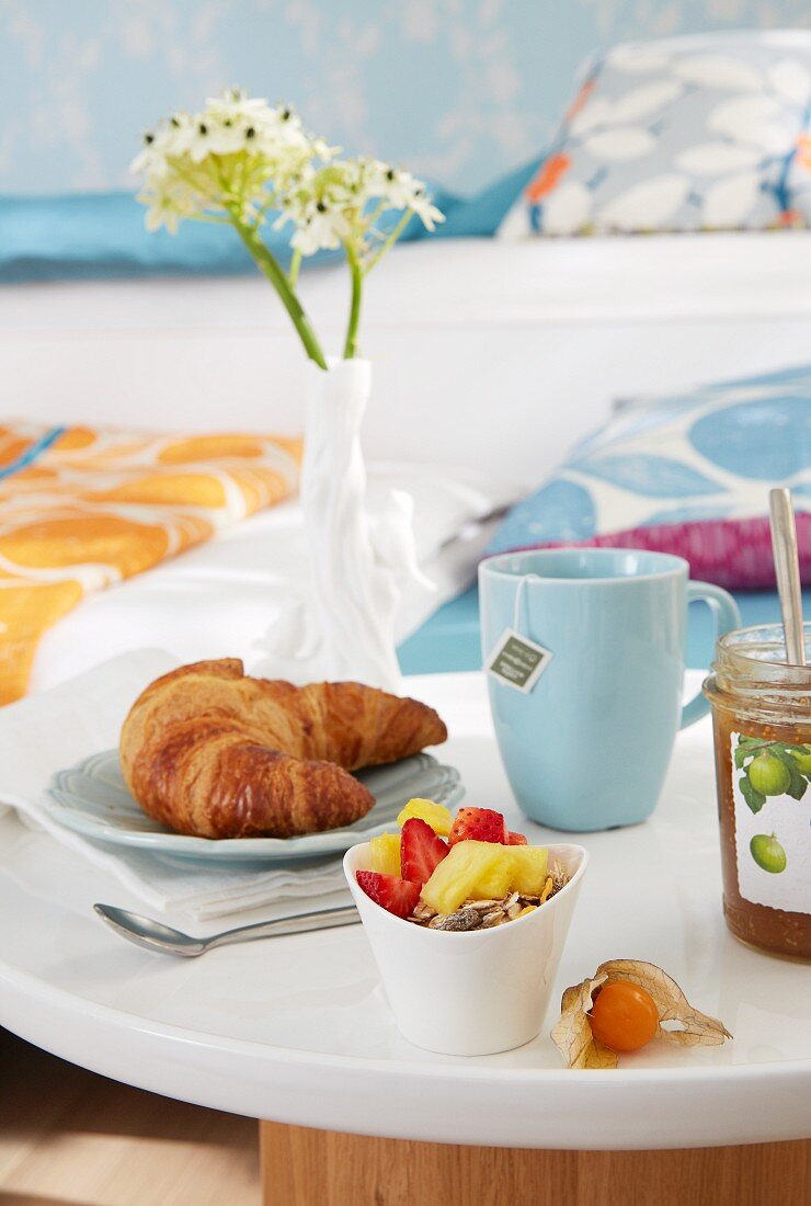 Frühstück mit Croissant und Obstsalat auf Tabletttisch am Bett