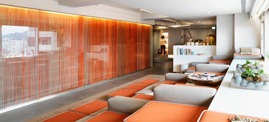 Lounge mit modernen Polstersesseln vor hinterleuchteter Glaswand mit Vorhang