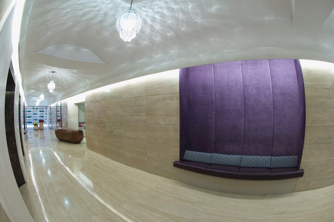 Polierte Steinfliesen an Wand und Boden und eingebaute Sitzbank mit lila Samtbezug in modernem Vorraum