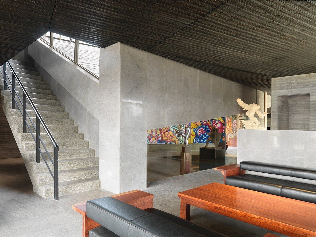 Minimalistische Halle mit Treppe in Betonausführung und Couchgarnitur vor Tisch aus Mahagoniholz