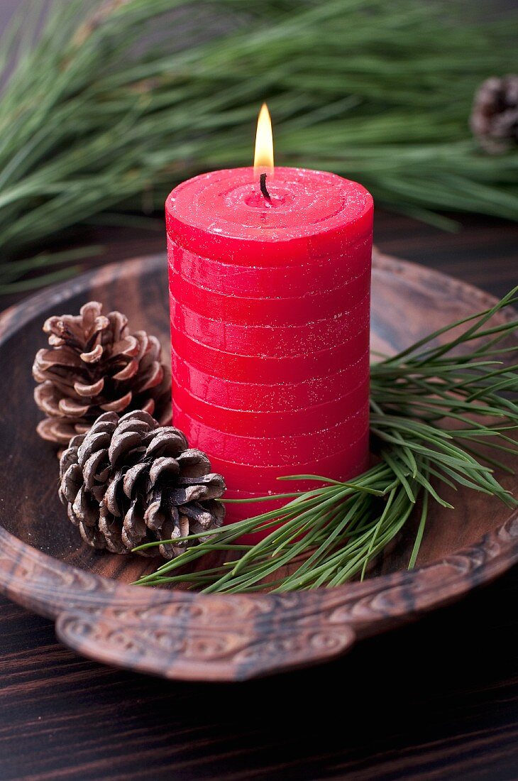 Red pillar candle with pinecones and pine twigs