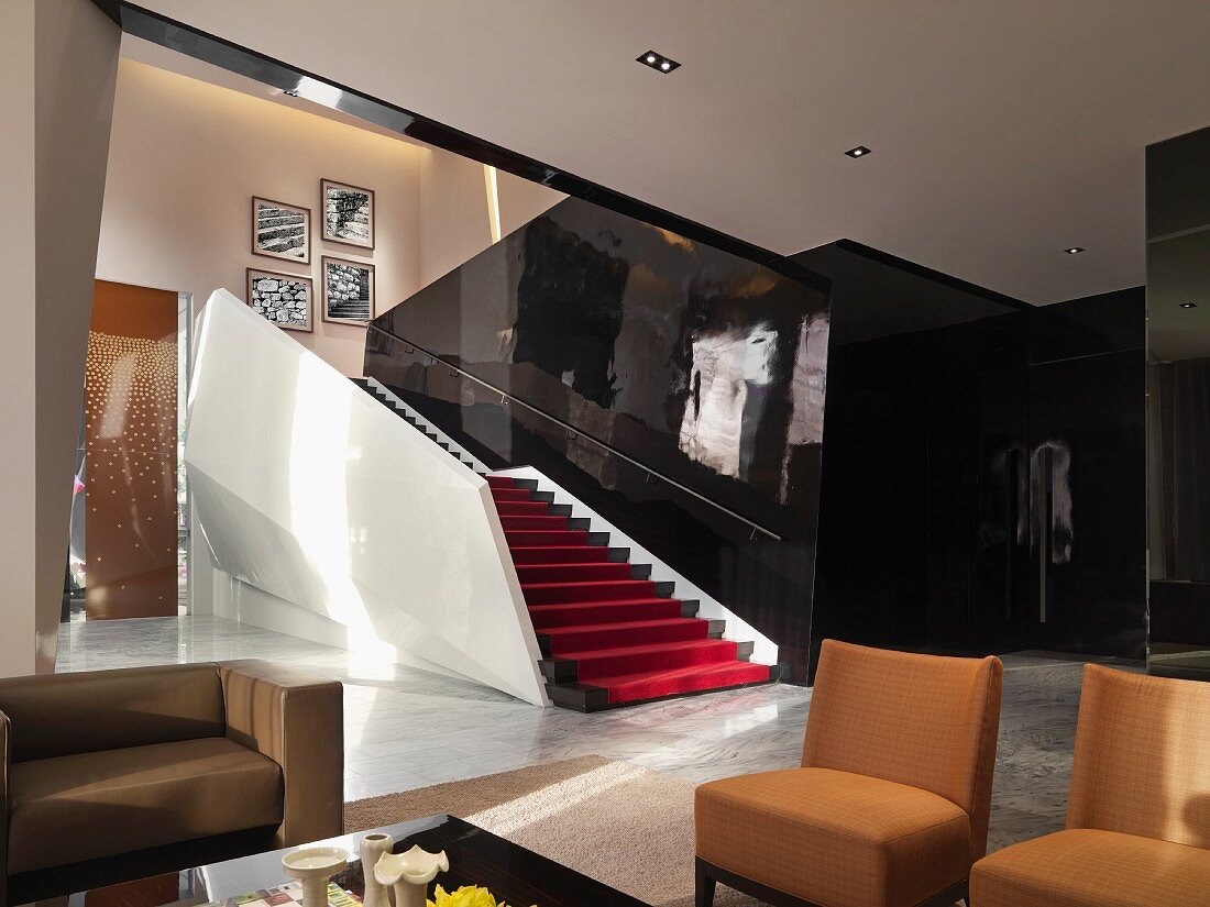 Braune Polsterstühle im modernen Wohnraum mit offenem Treppenaufgang vor schwarzer hochglänzender Wand