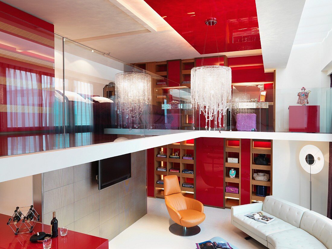 Blick von Galerie auf modernen Kronleuchter an roter Decke und in Wohnraum mit Polstercouch