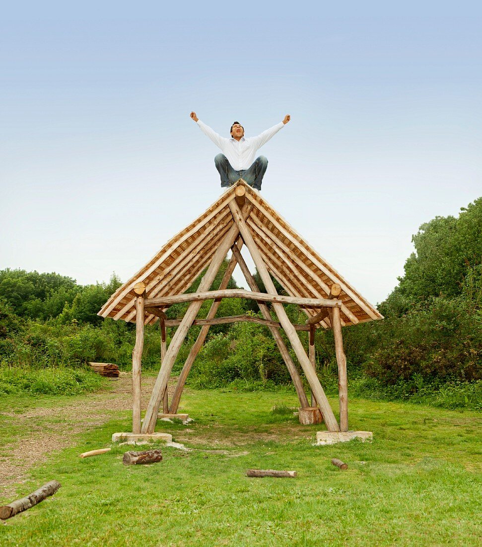 Man cheering on roof of log hut