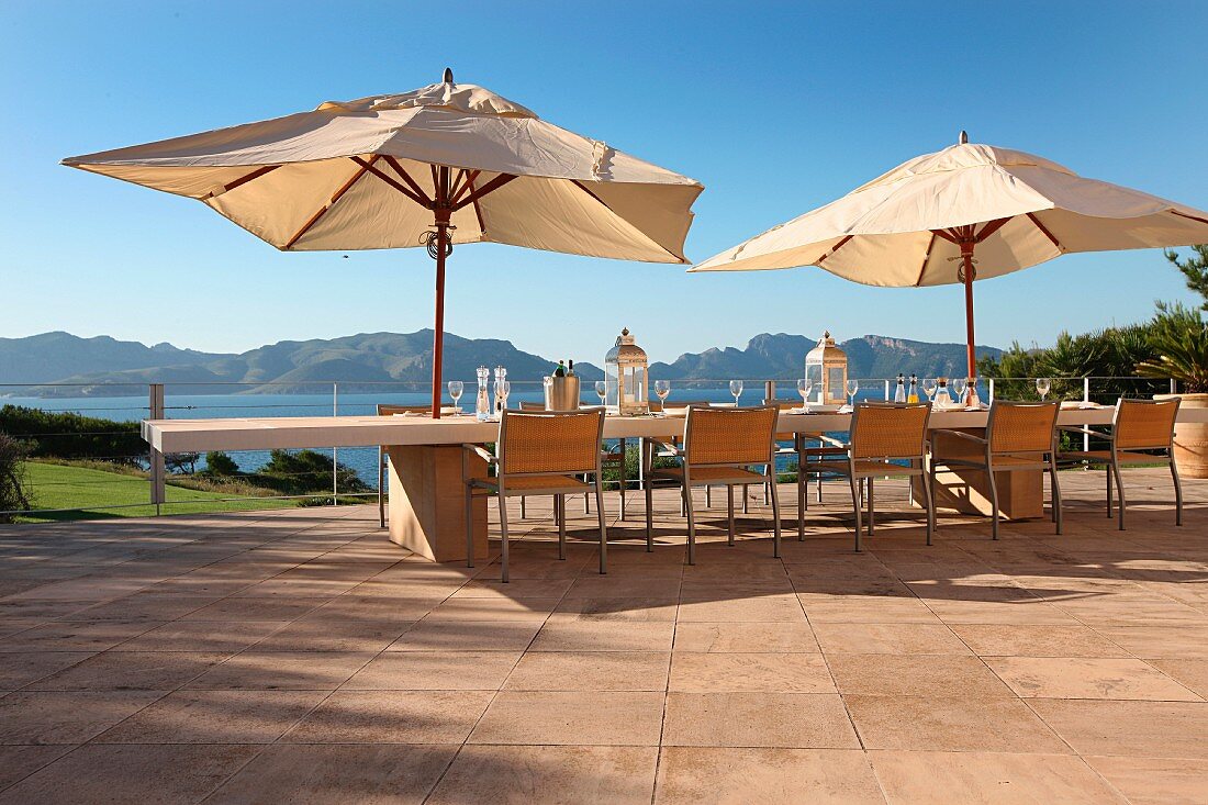 Gedeckter Tisch und Sonnenschirme auf Terrasse mit Meerblick