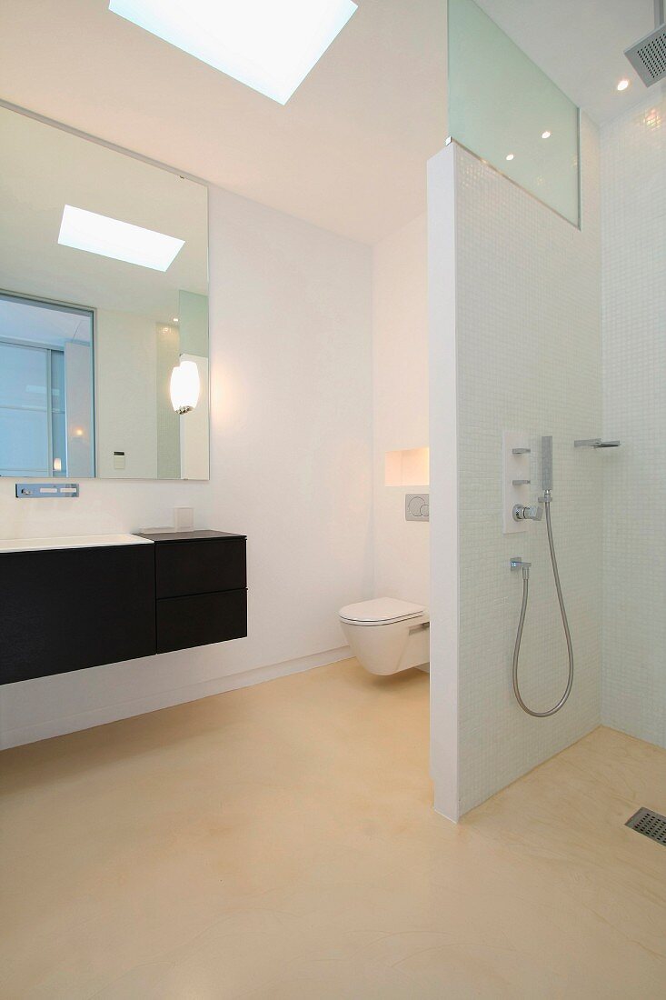 Weisses Designer-Bad mit Duschbereich und schwarzem Waschtisch vor raumhohen Spiegel