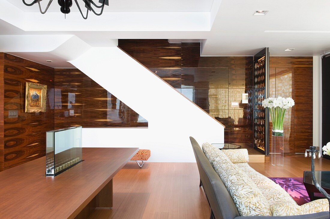 Esstisch und Sofa vor expressiv im Raum stehendem Treppen-Z; dahinter holzverkleidete Wände