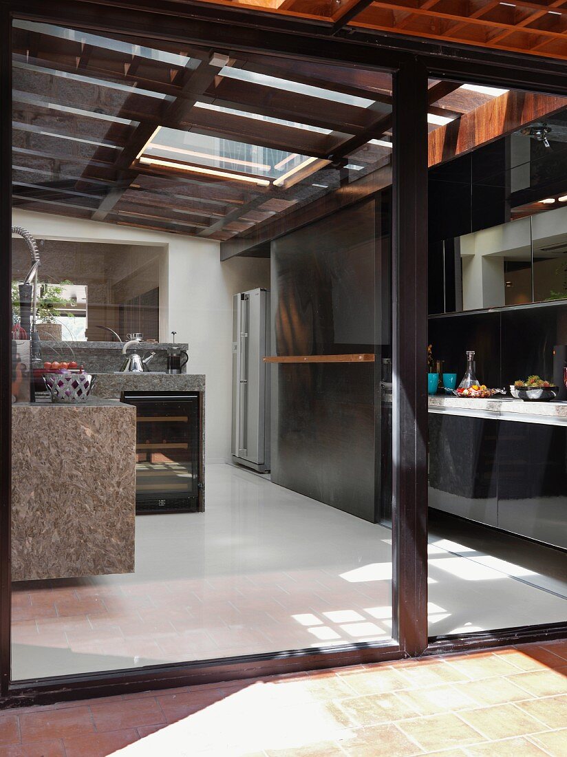 Designerküche mit natursteinverkleideter Küchenzeile unter einem Glasdach und Einbaufront mit Schiebeelement