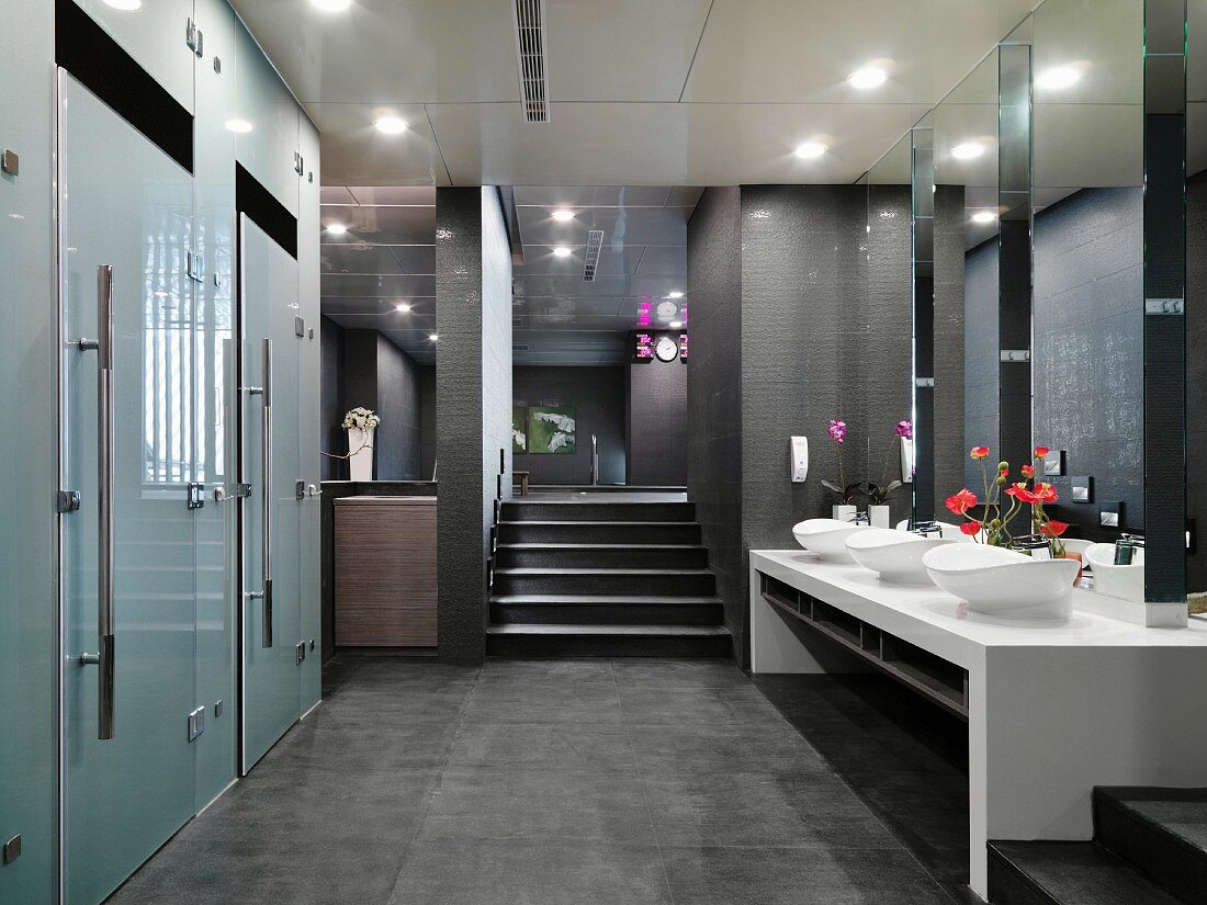 Grey and white interior in classic modern toilet anteroom with frosted glass doors and flower arrangements between oval washbasins