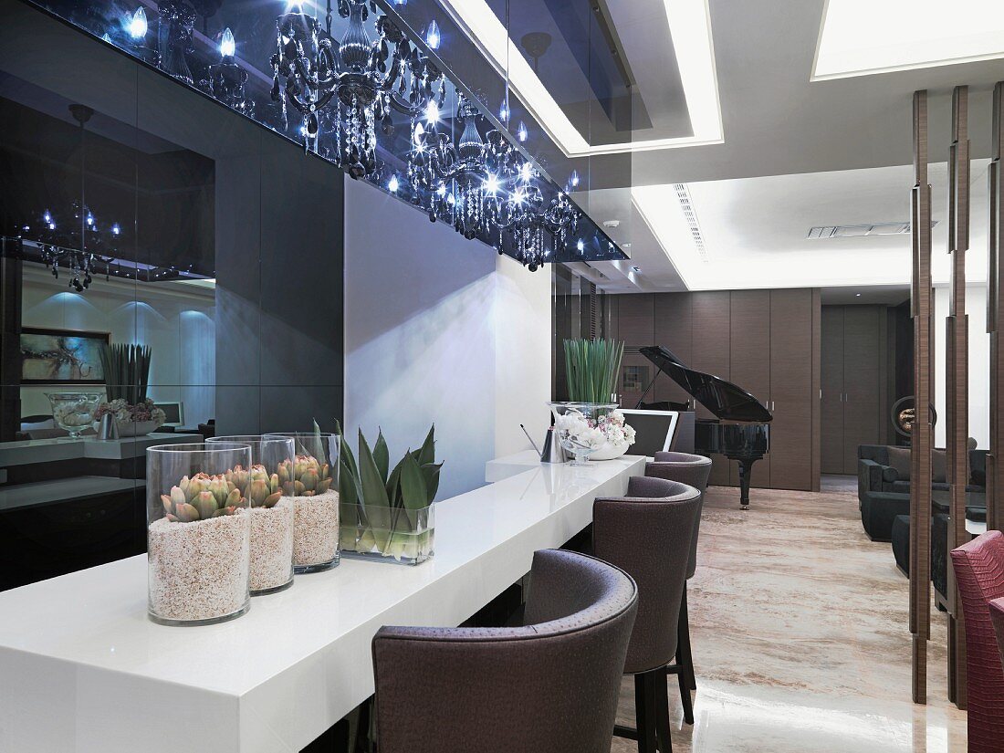 Classic modern lounge area and counter with leather stools below glittering chandeliers in blue light box of acrylic glass
