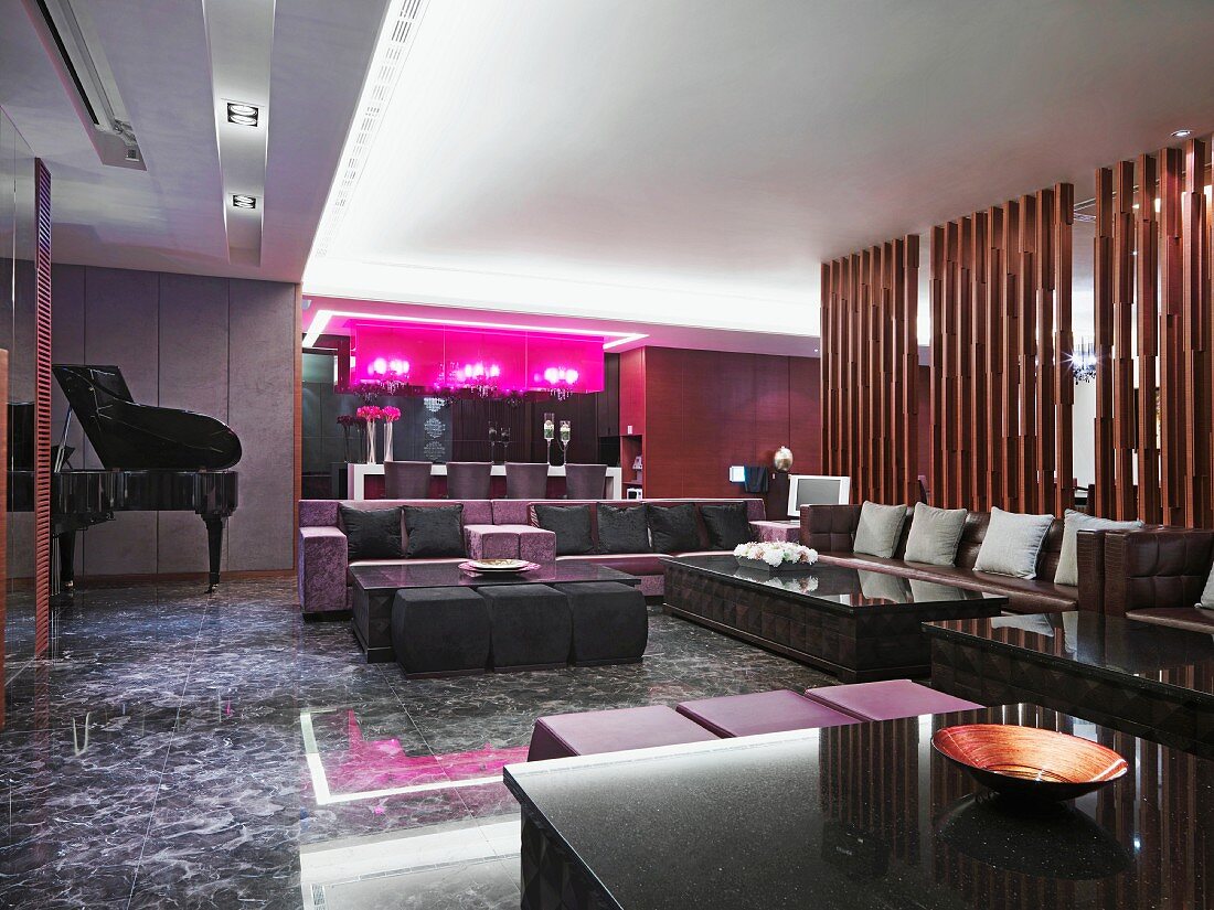 Extensive seating area with sofas, modern bar with hot pink light boxes and concert grand in classic modern hotel lounge
