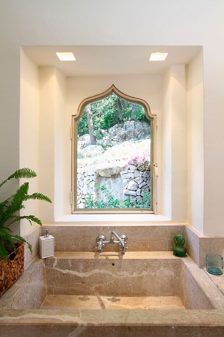 Waschbecken aus Stein vor Fenster mit Spitzbogen im maurischen Stil und Gartenblick