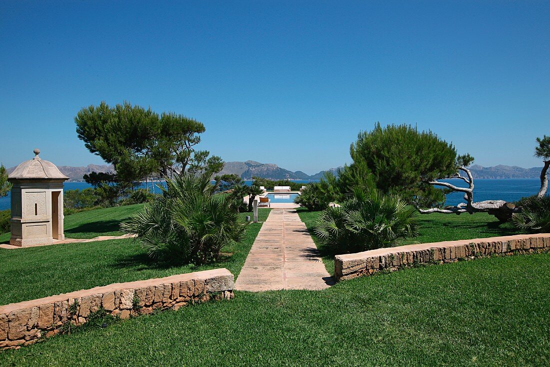 Mediterrane Gartenanlage mit niedriger Natursteinmauer und Blick auf das Meer