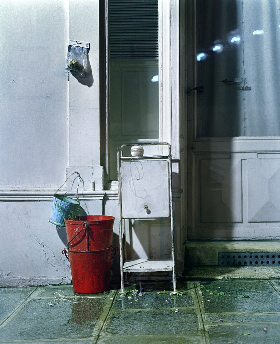 Small metal cabinet and buckets on wet stone floor against house wall