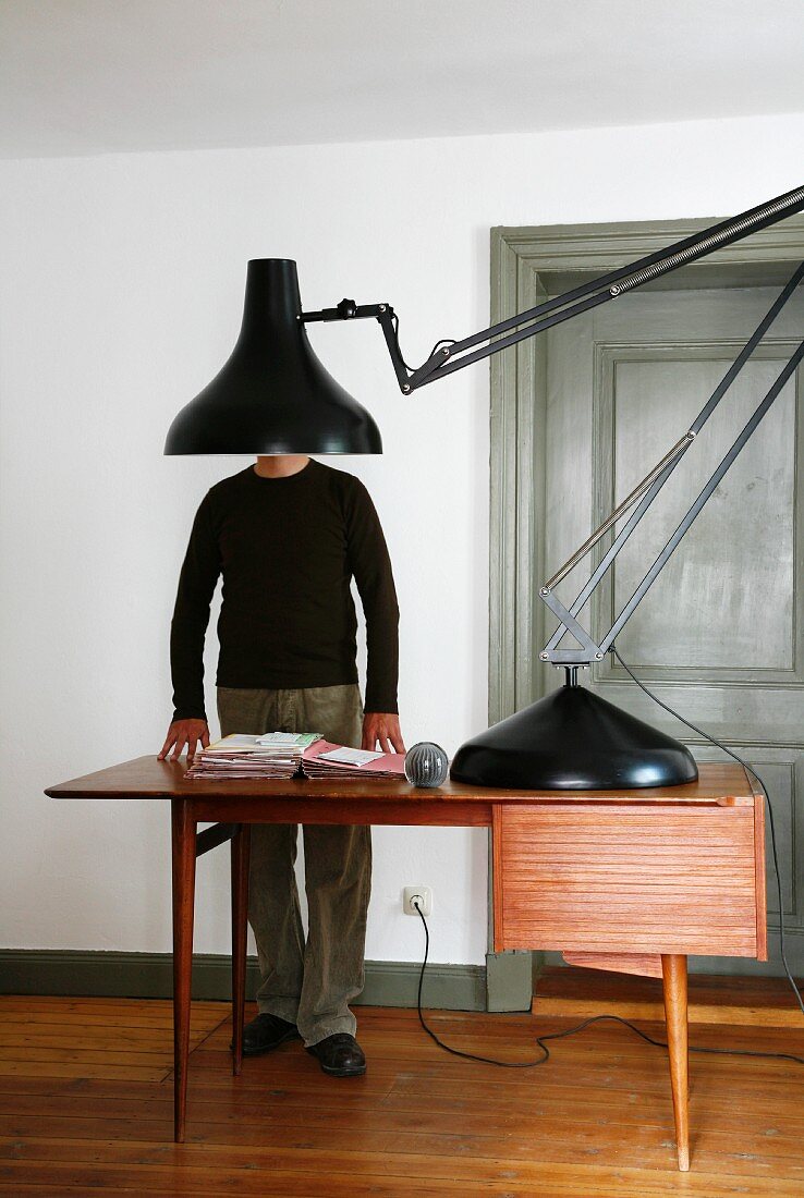 Überdimensionierte Retro Schreibtischlampe in Schwarz auf Arbeitstisch im Fiftiesstil und Mann im Hintergrund