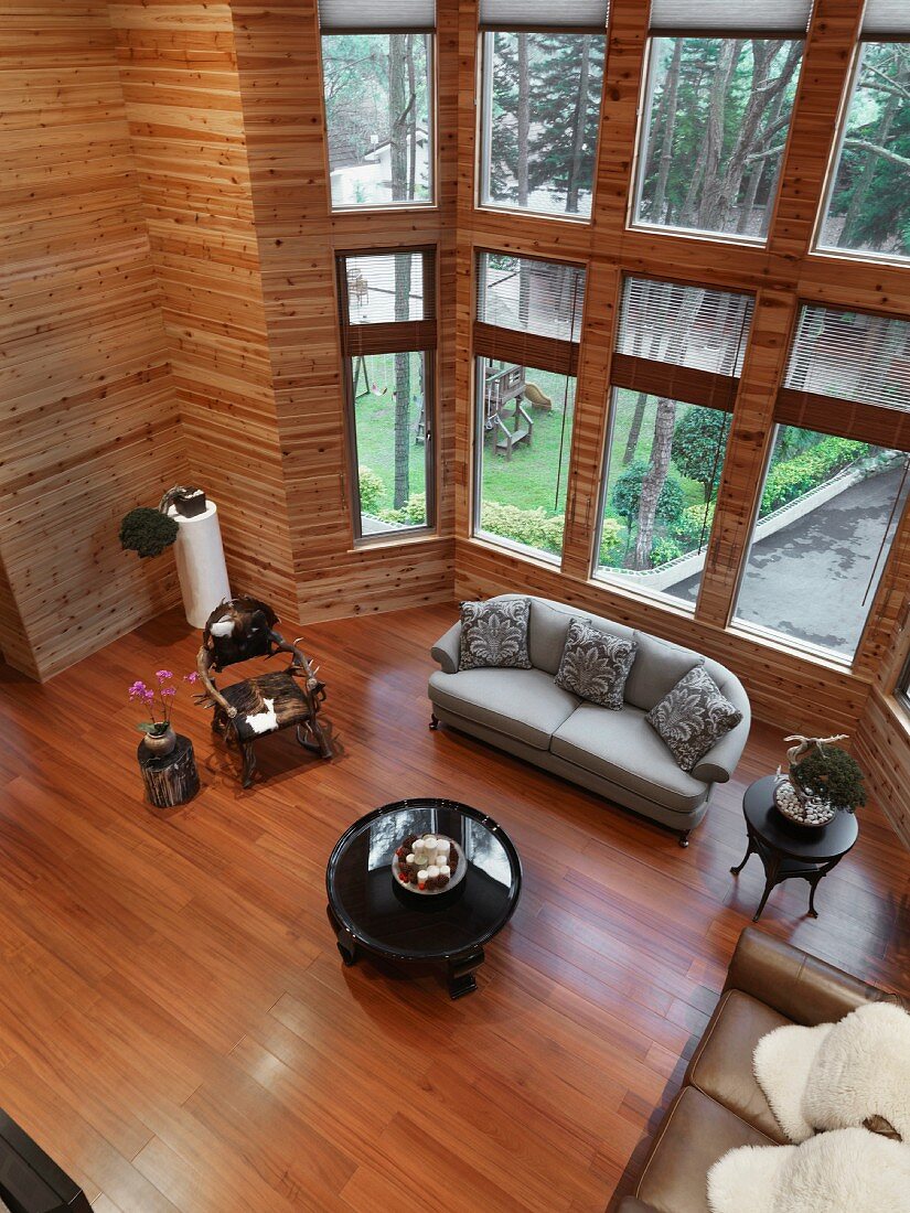 Blick auf hellgraues Sofa und Beistelltisch vor Fenster im offenen minimalistischen Wohnraum mit Holzverkleidung