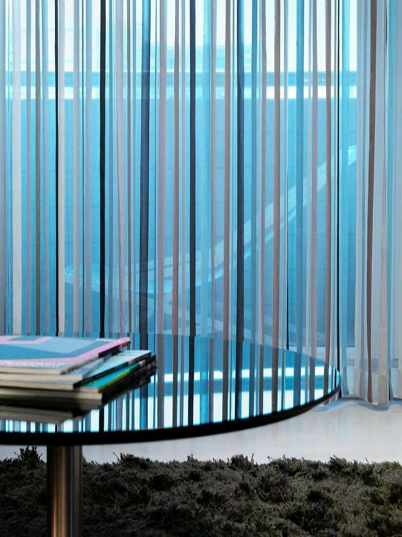 Round table with reflective surface in front of a mirror with a see-through curtain with a striped pattern