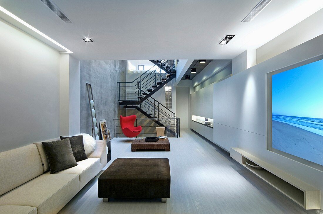 Moderne Loftwohnung mit hellem Sofa und gepolstertem Couchtisch im Wohnraum mit Blick auf offenes Treppenhaus