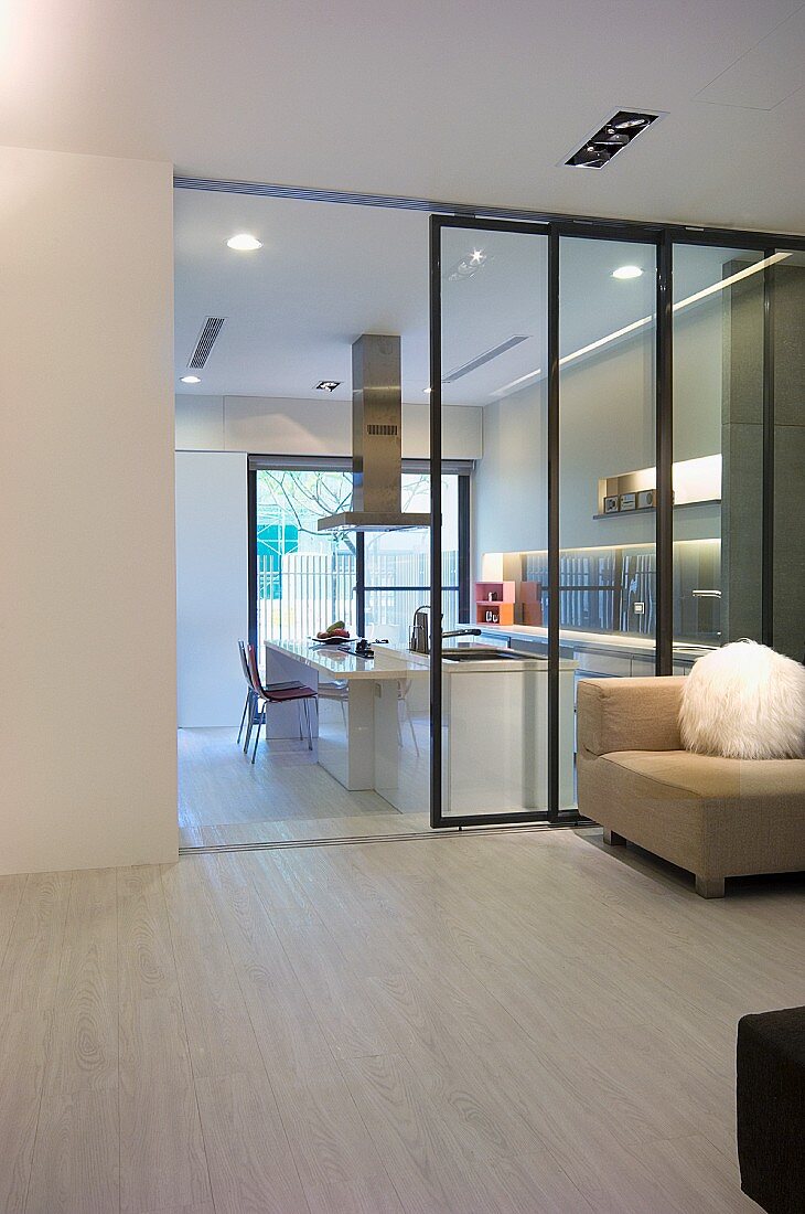 Sessel vor Glaswand im minimalistischen Vorraum mit Blick durch offene Schiebetür in weiße Designerküche