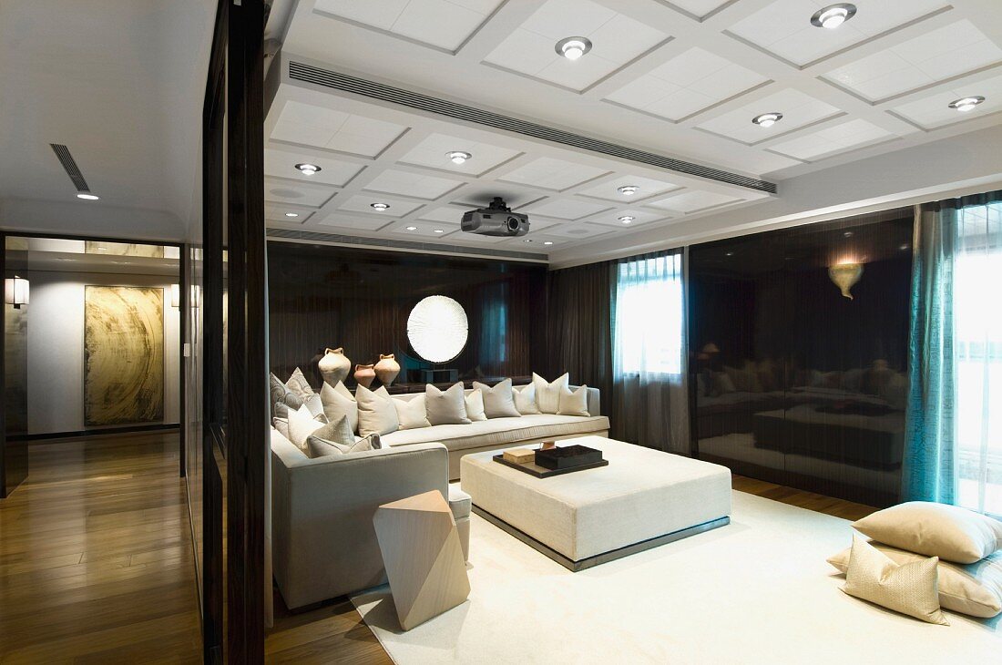 View into an elegant living room with a coffered ceiling and integrated lighting above a white living room suite in front of a black wall