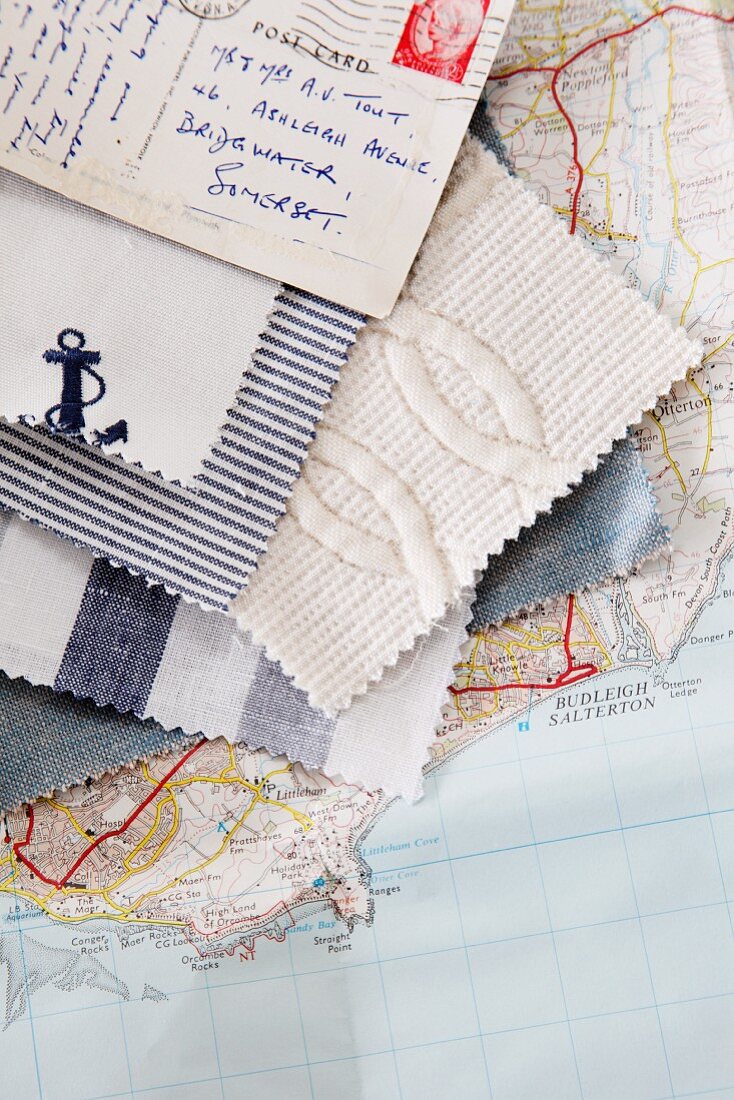 Stoffmuster für den maritimen Stil und frankierte Urlaubskarte, aufgefächert auf einer Landkarte