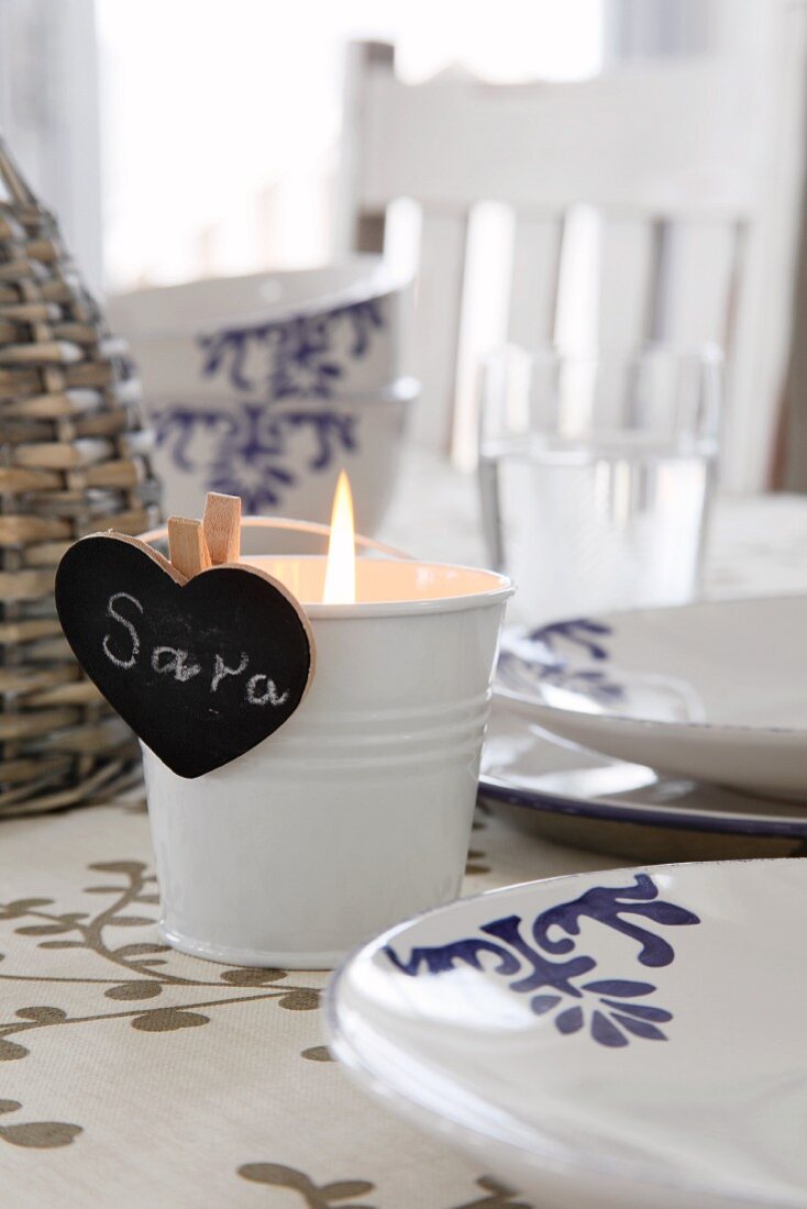 Lit tealight in metal bucket with heart-shaped, blackboard place name on set table