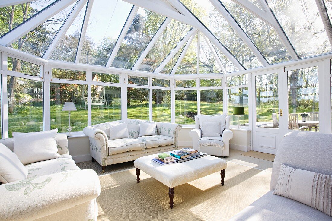 Spacious conservatory in extensive gardens; pale, traditional sofas and armchairs grouped around ottoman