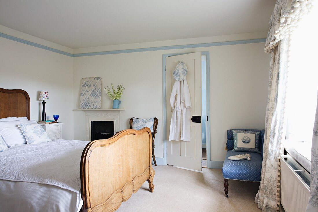 Antikes Doppelbett mit hohem Kopf- und Fussteil aus Naturholz und hellblau gemusterte Recamiere in lichtem Schlafzimmer mit Schabrackenvorhang im Nostalgieflair.