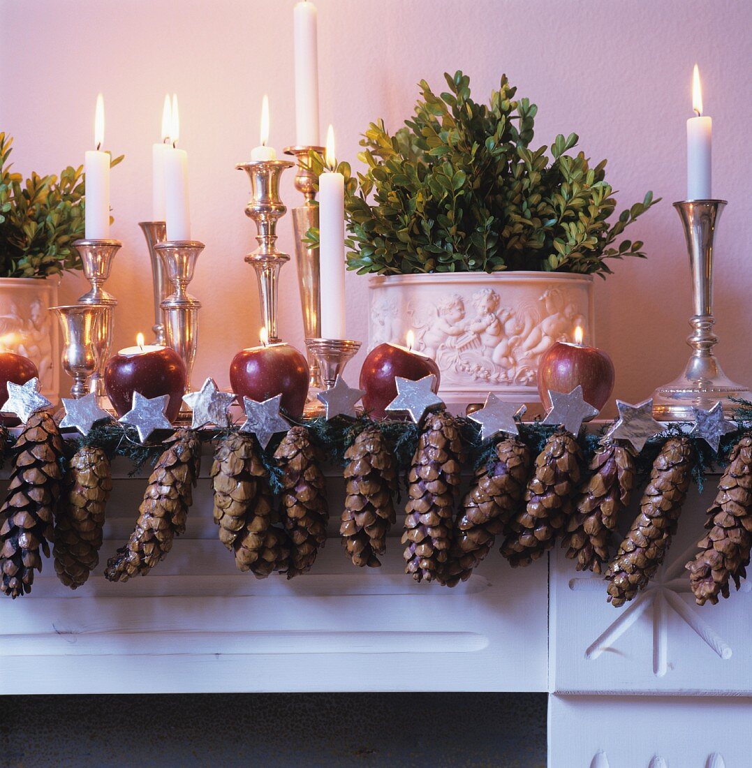 Festlich dekorierter Kaminsims mit Tannenzapfen und Kerzenständern mit brennenden Kerzen