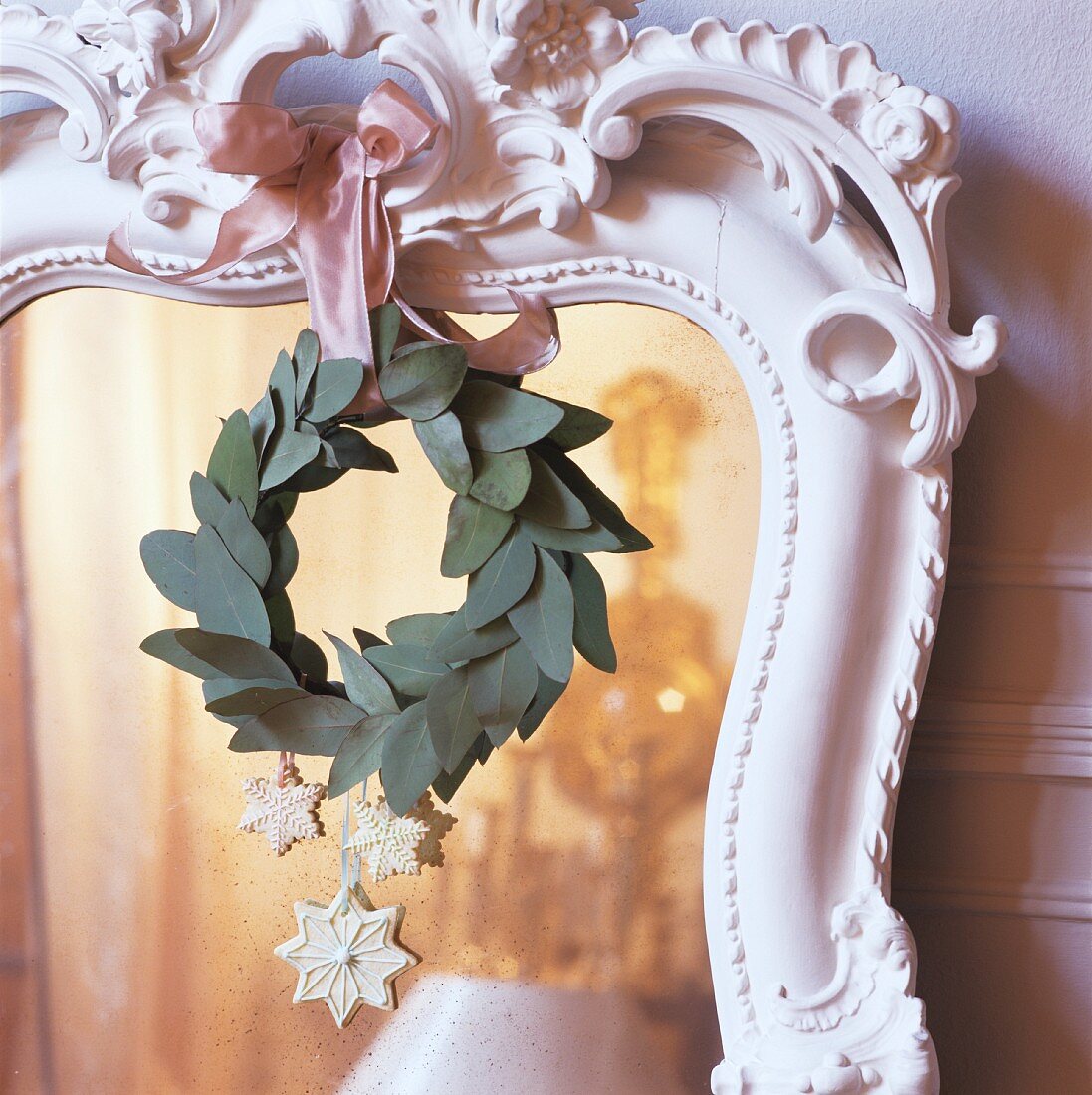 Weihnachtsdeko und Blätterkranz hängend an Spiegel mit weissen verziertem Holzrahmen