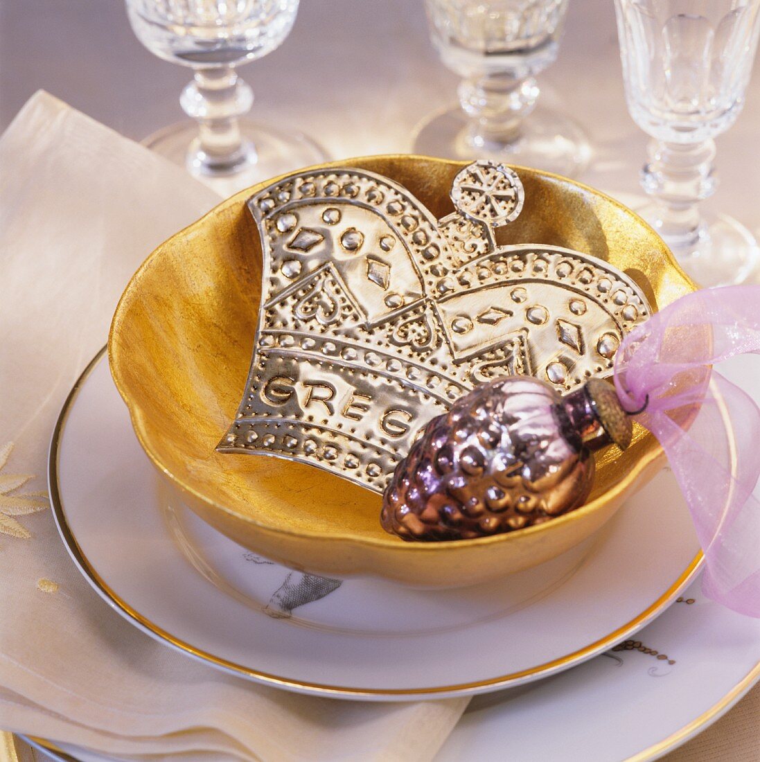 Christmas decorations in gold bowl on place setting with crystal glasses