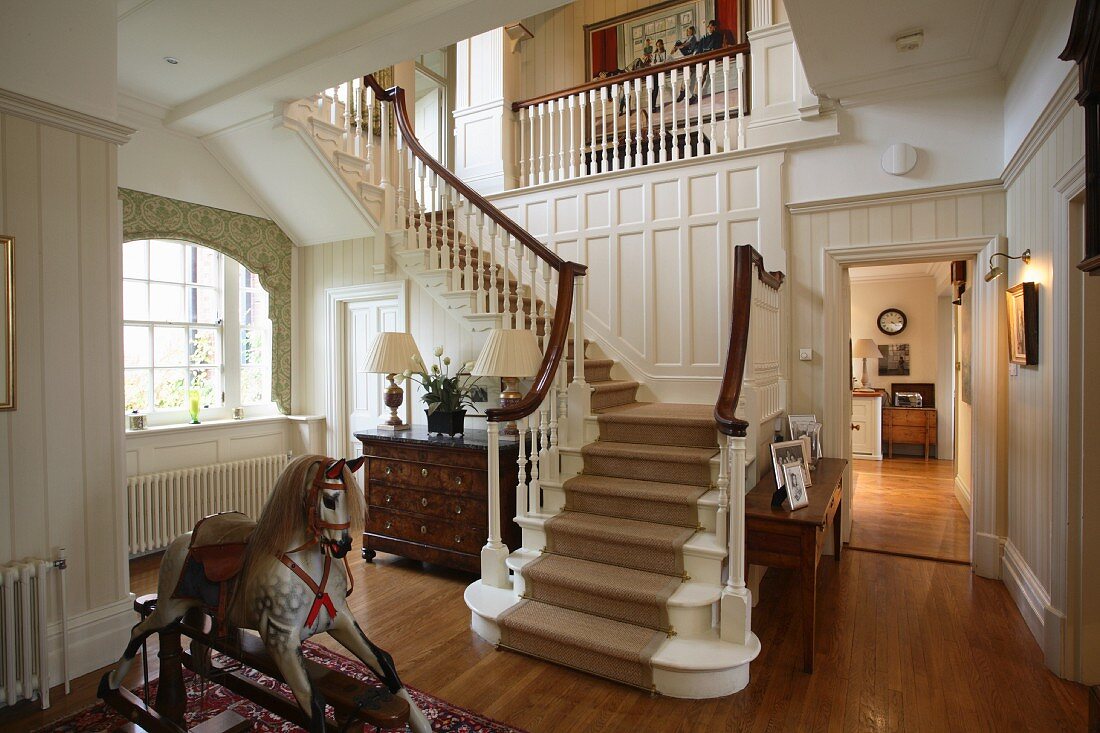 Antikes Schaukelpferd vor weiss lackierter Holztreppe in der grosszügigen Diele eines elegant gemütlichen Landhauses mit Parkettboden.