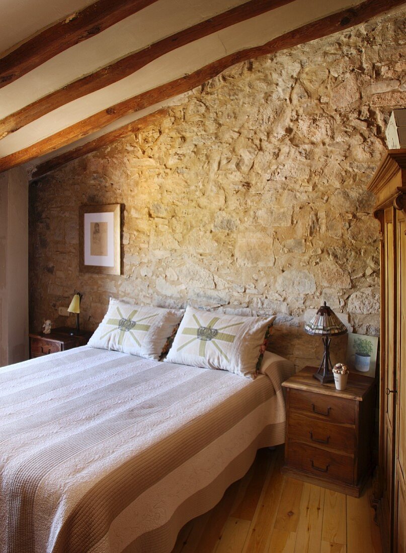 Doppelbett mit Nachtkästchen vor Natursteinmauer in mediterran-rustikalem Schlafzimmer