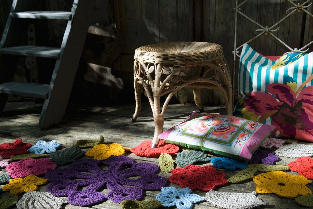 Crocheted flowers in various colours and colourful scatter cushion on wooden floor in front of wicker stool