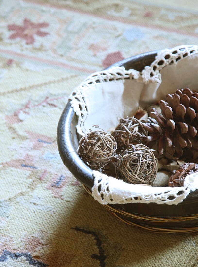 Fir cones and balls of twigs in dish with crochet-edged doily on kilim rug