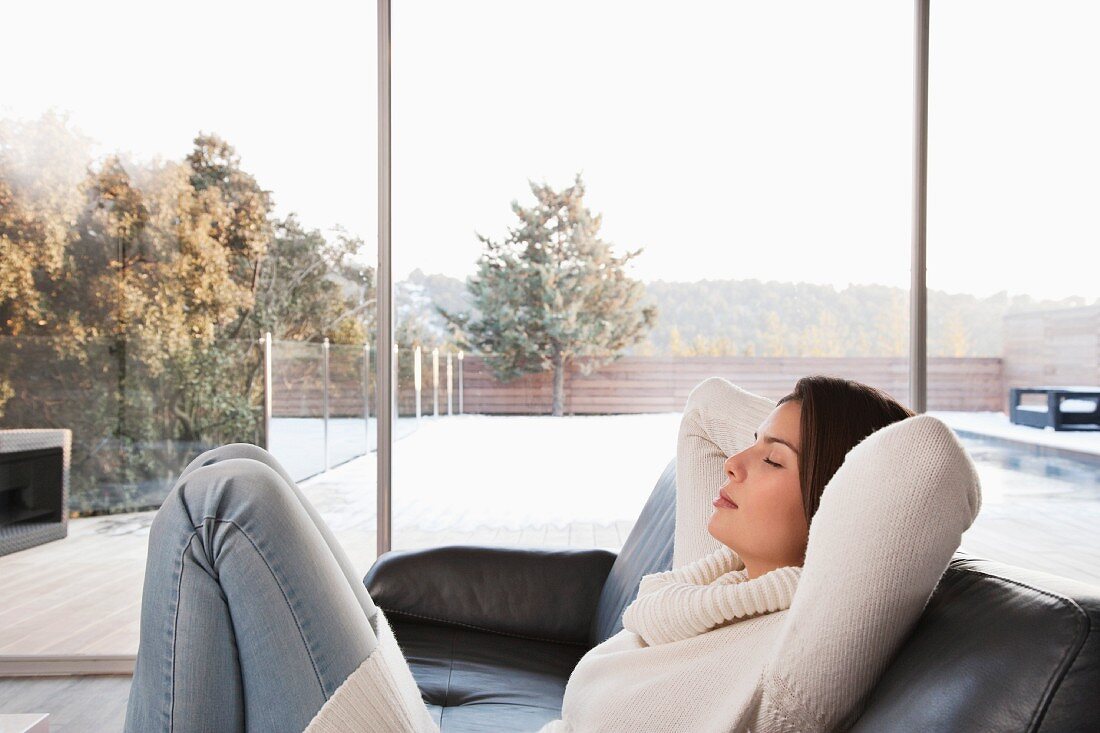 Junge Frau entspannt sich auf dem Sofa vor dem Terrassenfenster