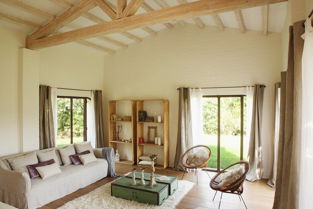 Gemütliches Polstersofa und Retro Stühle im Wohnzimmer eines mediterranen Hauses mit sichtbarem Dachstuhl
