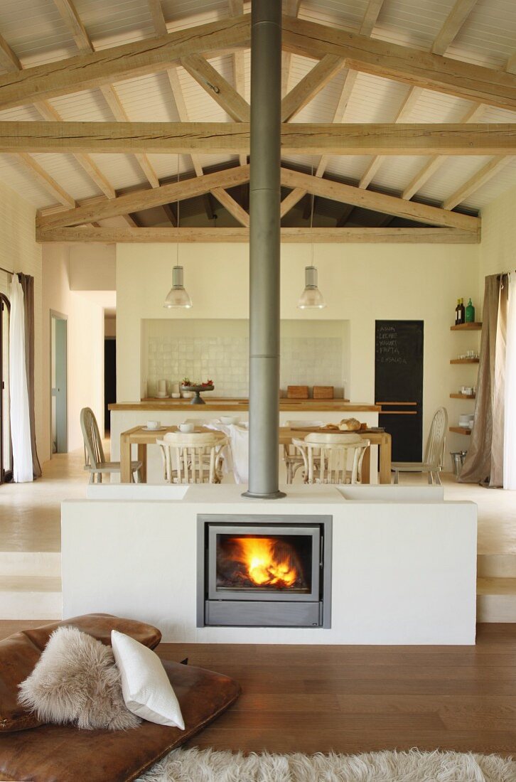 Eingebauter Kamin in Wohnzimmermitte vor Essbereich und Küche auf Podest in offenem, mediterranem Haus