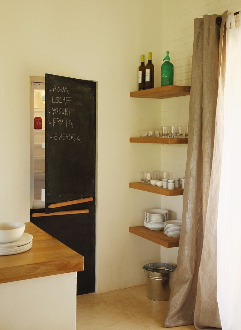 Corner of modern kitchen - fitted fridge-freezer with blackboards on doors next to crockery on shelves