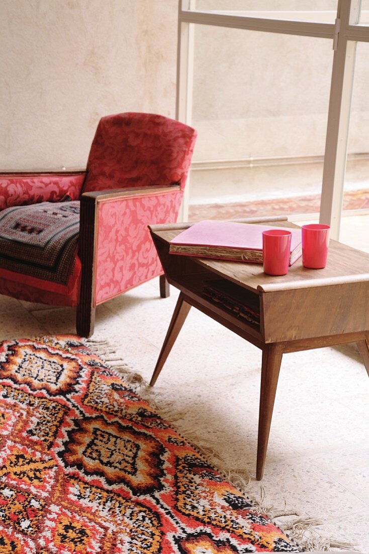 Beistelltisch aus Holz im Fiftiesstil neben traditionellem Sessel und gemusterter Teppichläufer