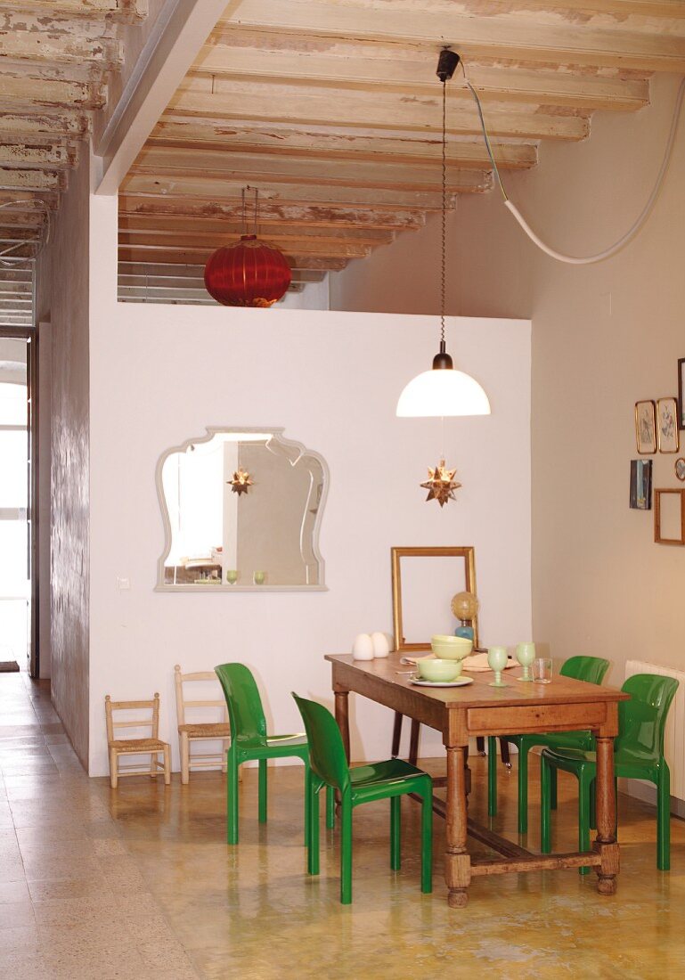 Green plastic chairs around wooden table next to wall of module installed in loft-style interior