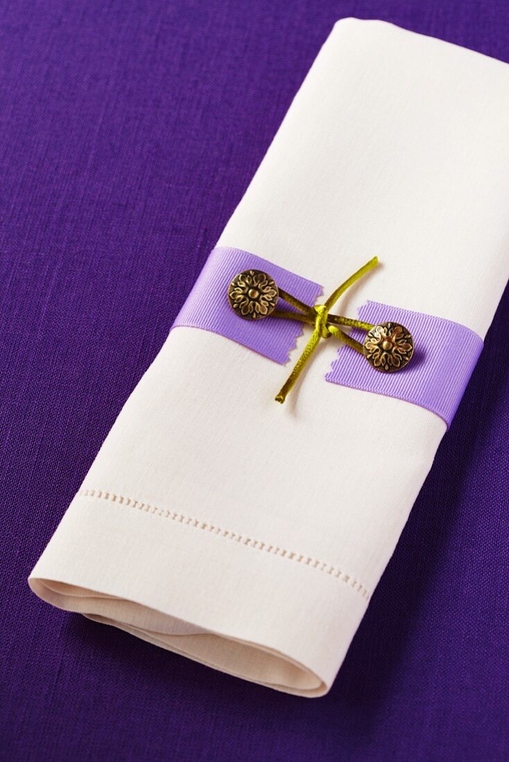 weiße Leinenserviette mit Serviettendeko auf einer violetten Leinentischdecke