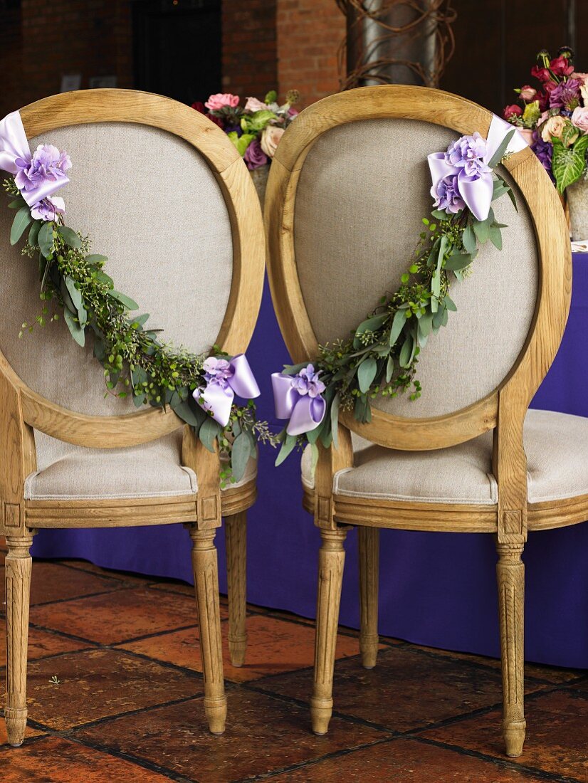 Chairs Decorated with Fresh Garland and Ribbon for the Bride and Groom at a Wedding Reception