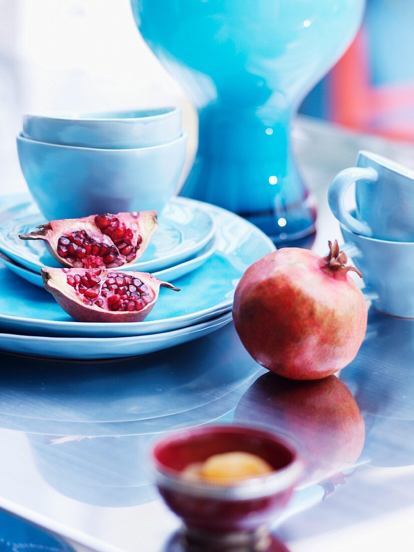 Granatäpfel und pastellblaues Keramikgeschirr auf glänzender Tischplatte