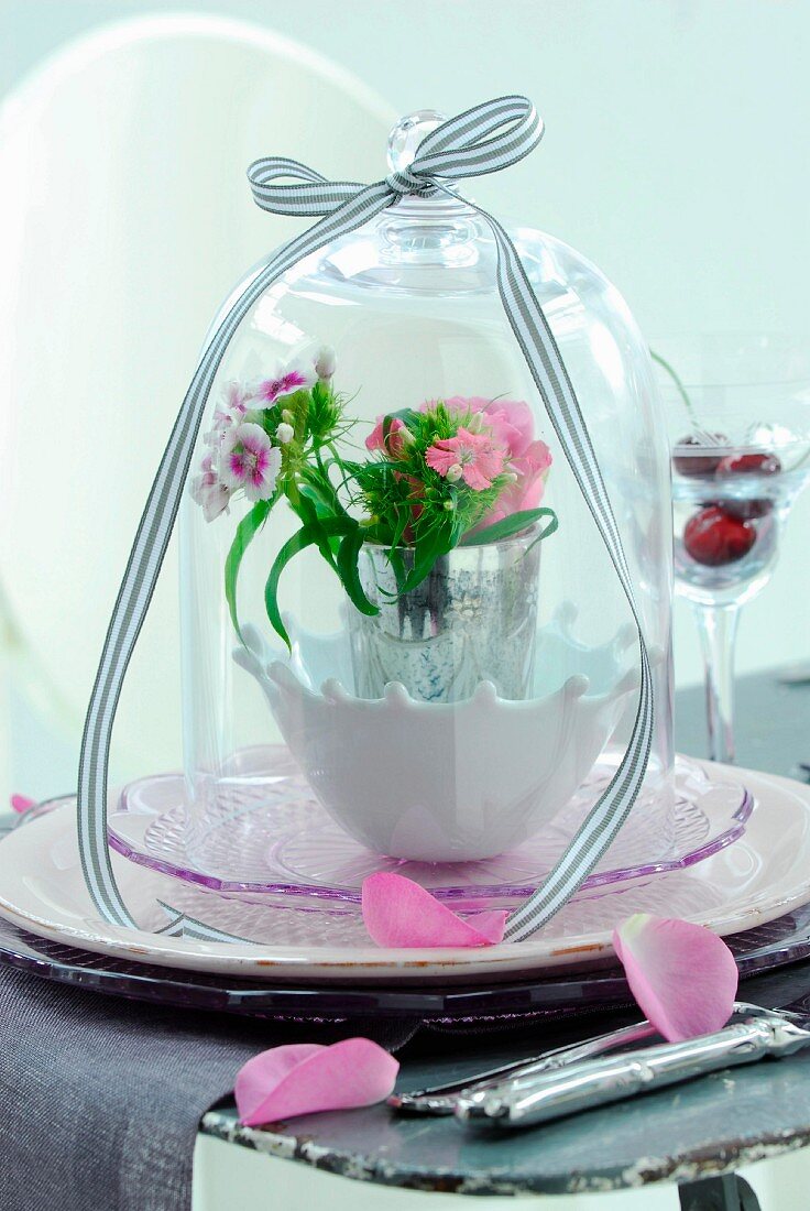 Frühlingsstrauss in Vase unter Glashaube auf Schalen