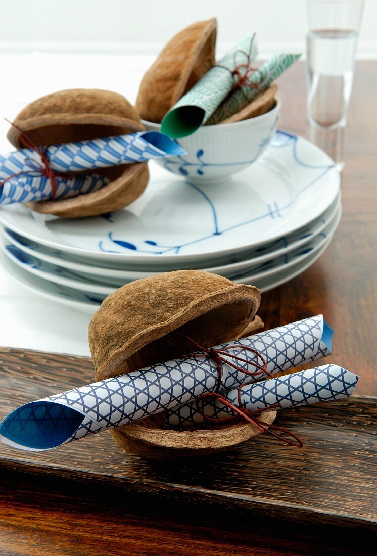 Gerolltes Origamipapier in Deko-Nussschalen und Teller mit weiss-blauer Bemalung auf dem Tisch